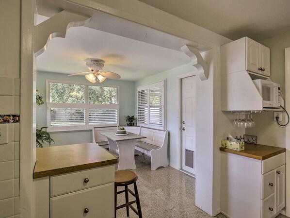 A kitchen with a wooden countertop, white cabinets, a microwave, and a ceiling fan.