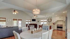 A modern kitchen with white cabinetry, a central island, and a dining area with white chairs and a round table. - 2 Blocks from Beach, Dog Friendly w/ no dog fees!, Hot Tub, Fenced Yard (Kure Beach)