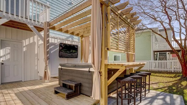 A wooden deck with a hot tub, two wicker chairs, and a pergola structure. - 2 Blocks from Beach, Dog Friendly w/ no dog fees!, Hot Tub, Fenced Yard (Kure Beach)