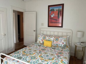 Un dormitorio con cama, una puerta, un cuadro en la pared y una mesita de noche.