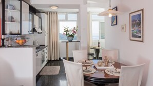 A modern kitchen with a dining area, featuring a large window, a vase with flowers, and a table set for four. - Sea View Apartments - Apartment Merivo (Dubrovnik)
