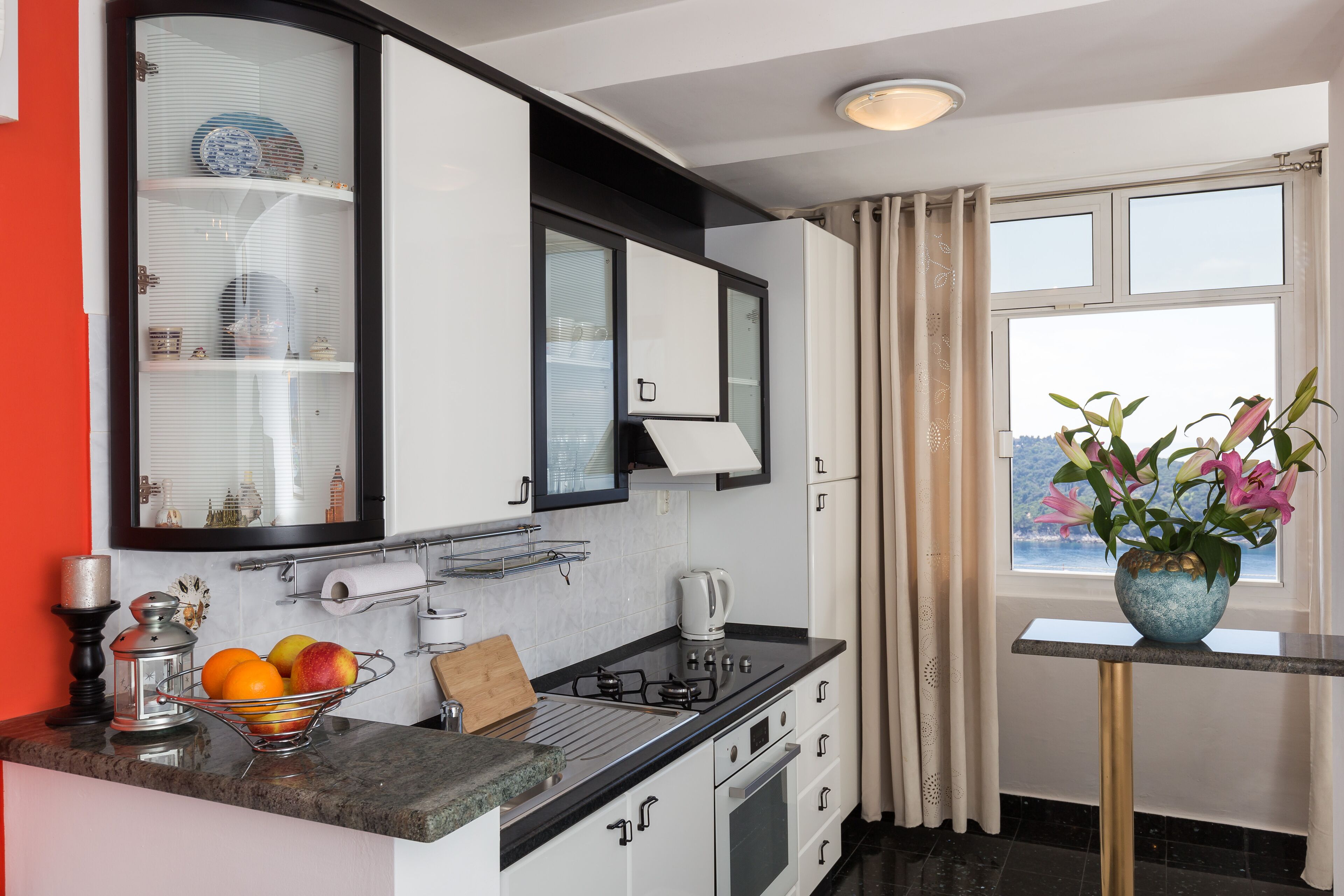 A modern kitchen with a gas stove, a sink, and a window with curtains.