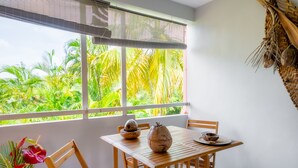 Una mesa de madera con sillas, una ventana con persianas y vistas a exuberante follaje.