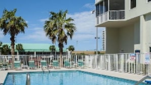 A swimming pool with a white fence, palm trees, and a building with balconies. - LOWER LAST MINUTE WEEKDAY PRICE!! Come relax in Destin without the crowds! (Destin)