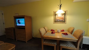 A dining area with a wooden table and chairs, a television on a wooden cabinet, and a framed picture on the wall. - LOWER LAST MINUTE WEEKDAY PRICE!! Come relax in Destin without the crowds! (Destin)