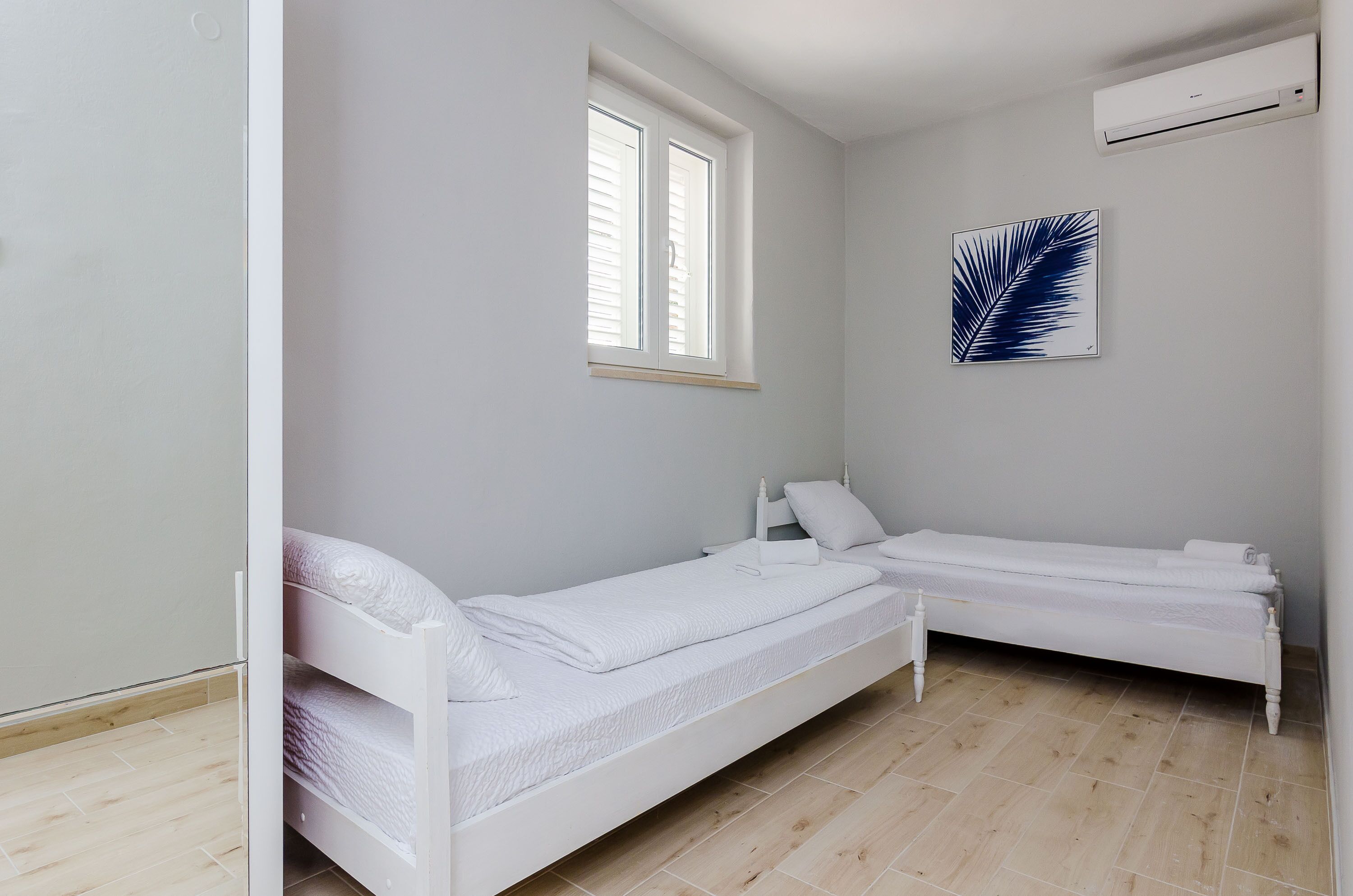 Ein kleines, sauberes Zimmer mit zwei weißen Betten, einem Fenster und einer Wand-Klimaanlage.