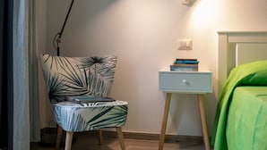 Een slaapkamer met nachtkastje, stoel, bed en schilderij aan de muur.