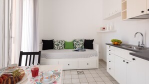 Een ruimtelijk ingerichte leefruimte met kitchenette, eethoek en bed.