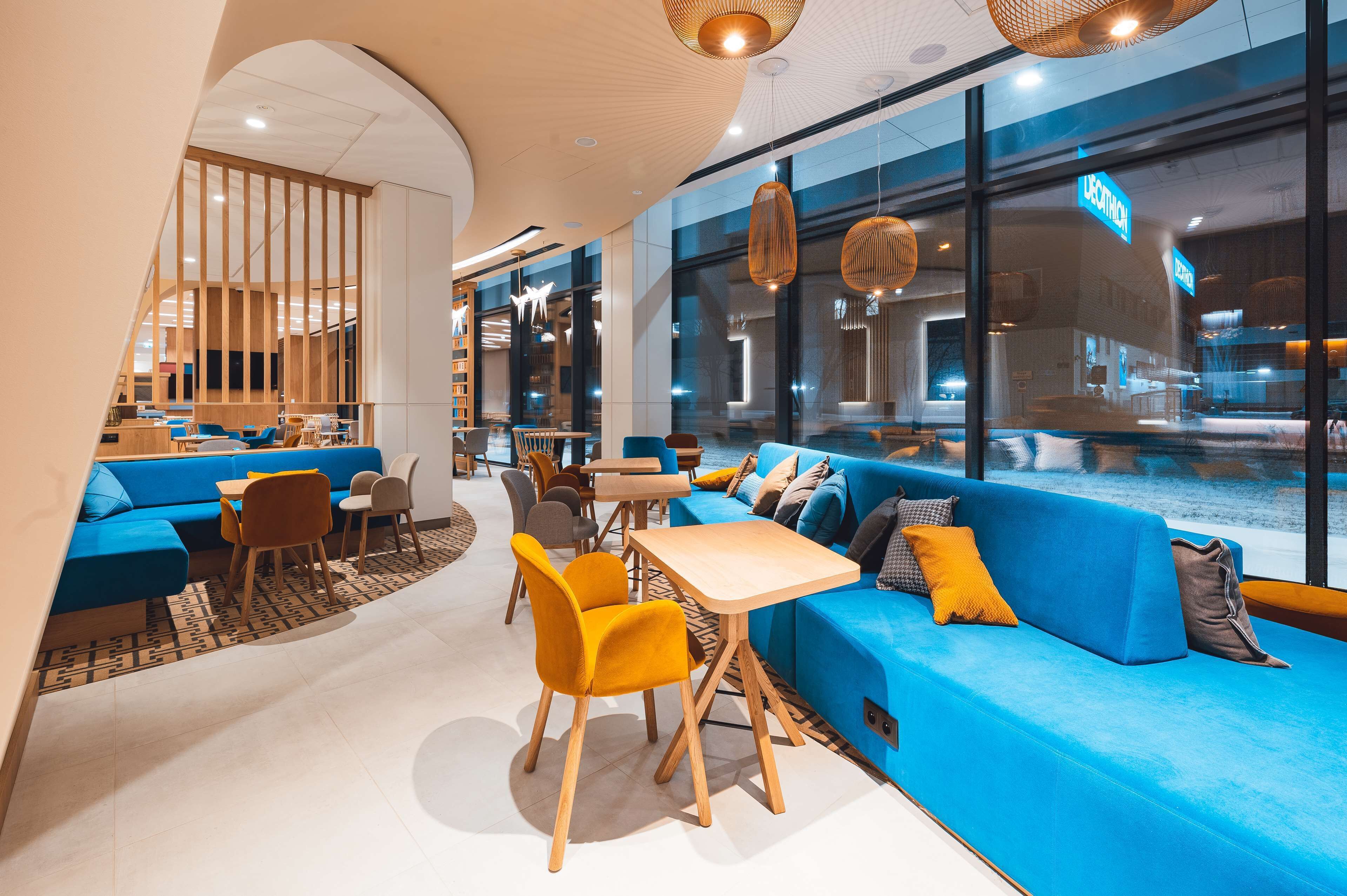 Un espace de détente moderne avec des sièges bleus, des tables en bois et des luminaires suspendus.