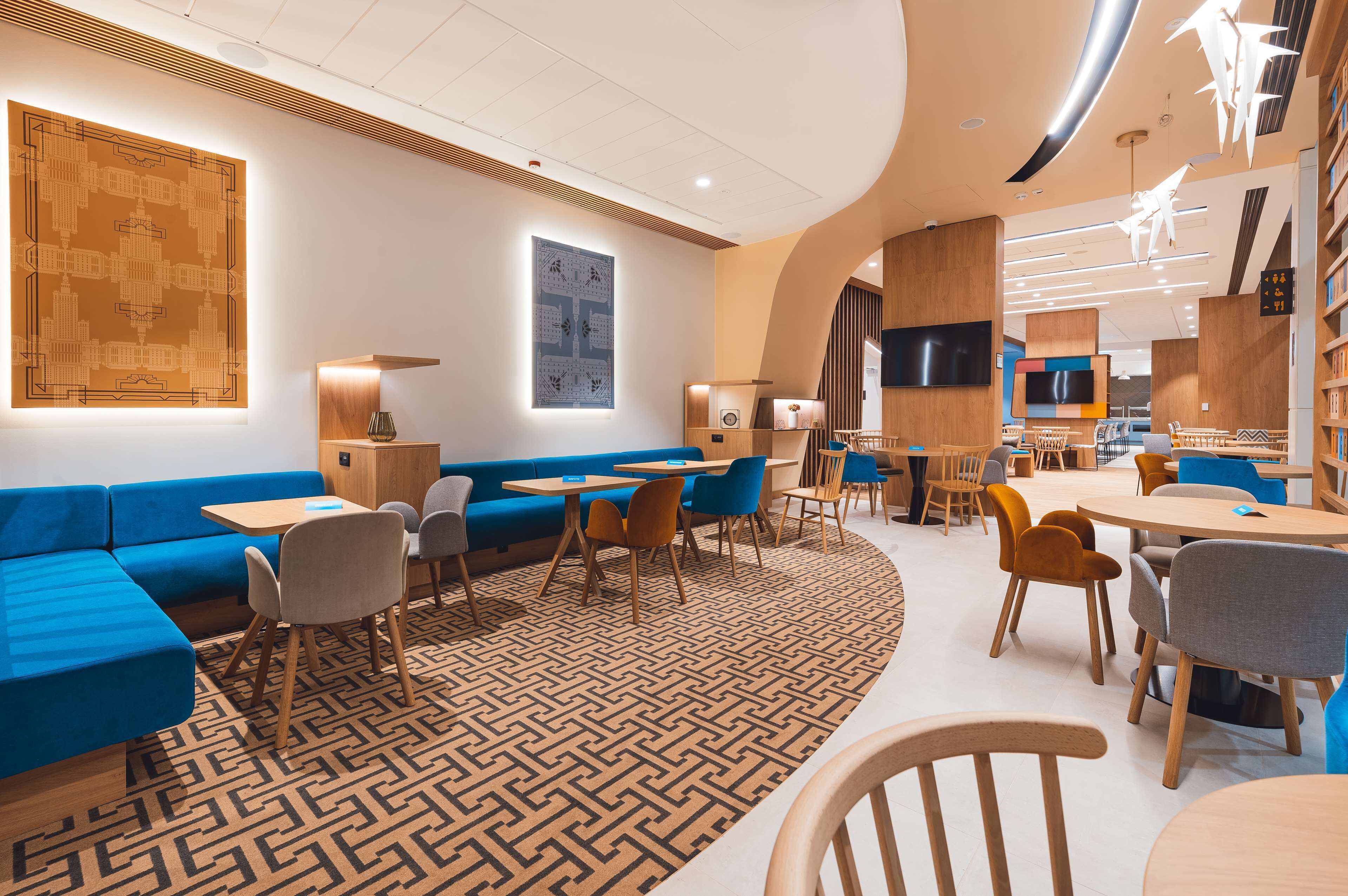 A modern library with blue seating areas, wooden tables, and bookshelves.