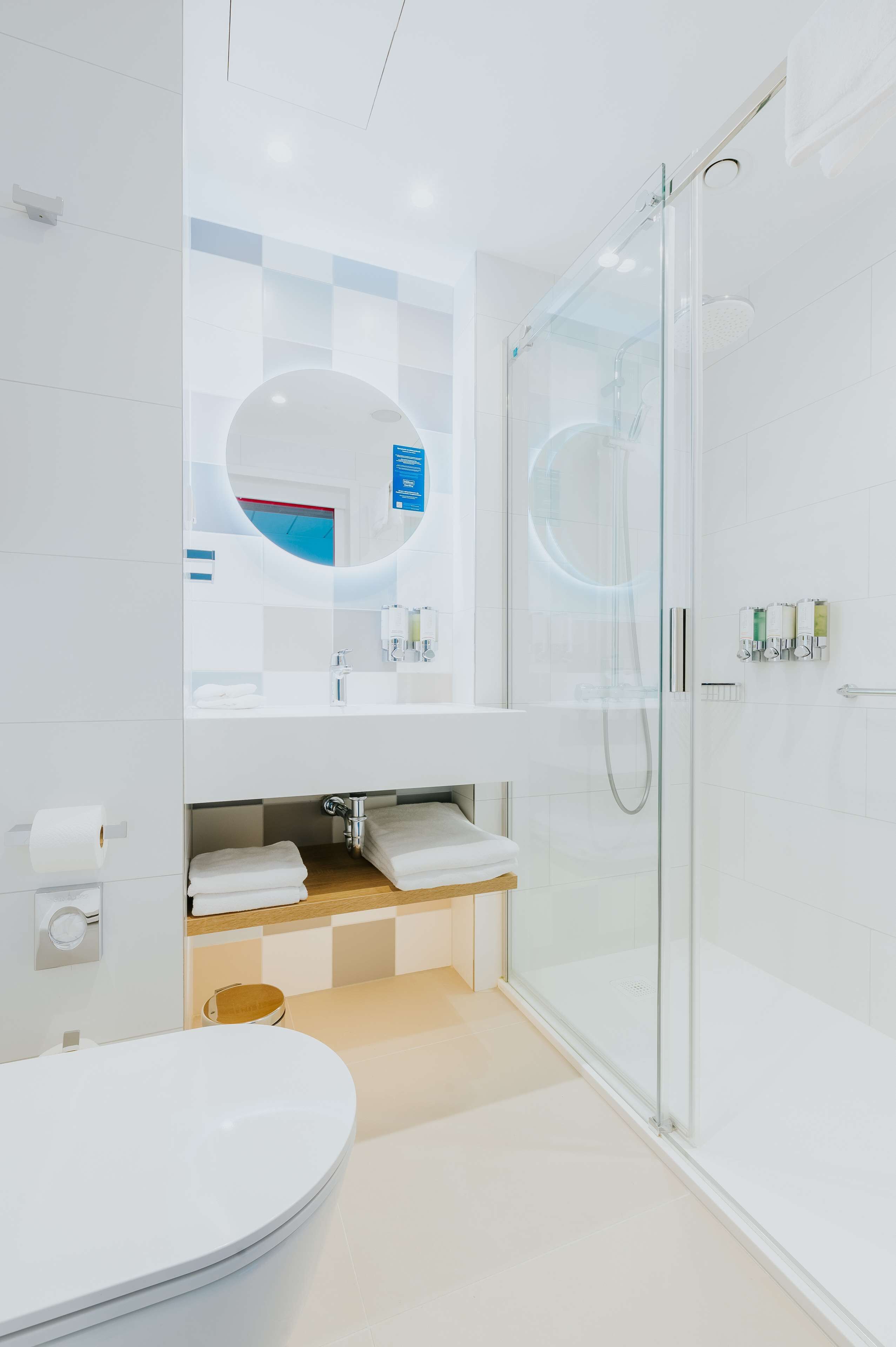 A modern bathroom with a glass-enclosed shower, a white sink with a mirror, and a round mirror above the sink.