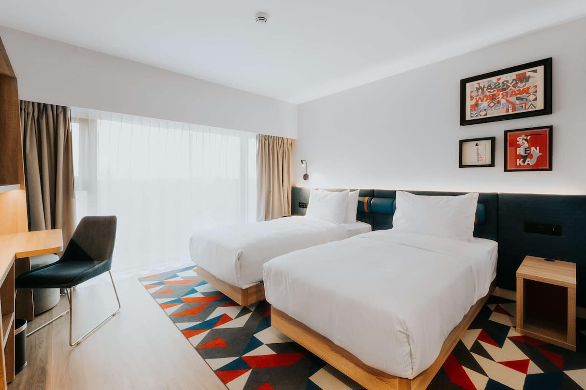 A hotel room with two beds, a desk, a chair, and a small table.
