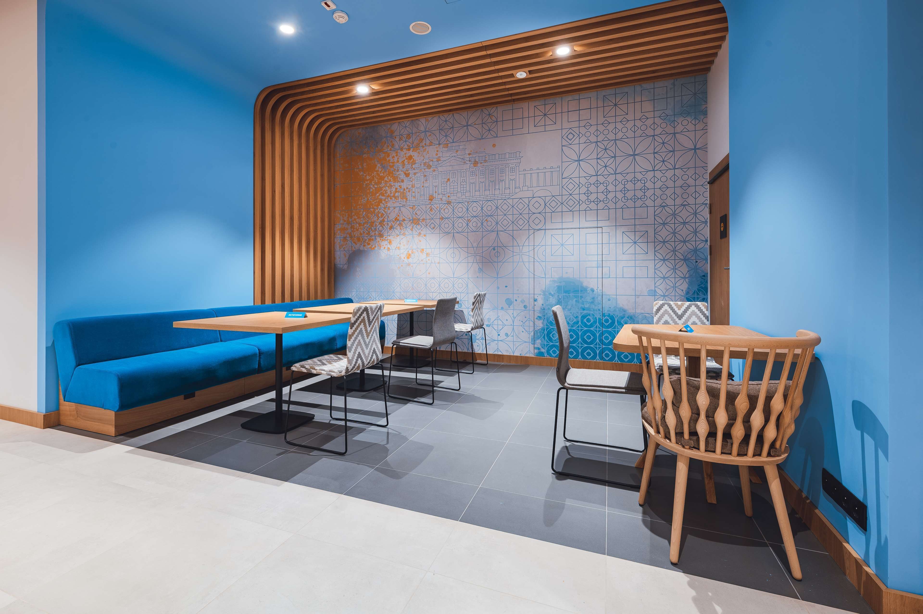 Ein modernes Café mit blauen Wänden, Holzelementen und einer Wandmalerei mit Muster.