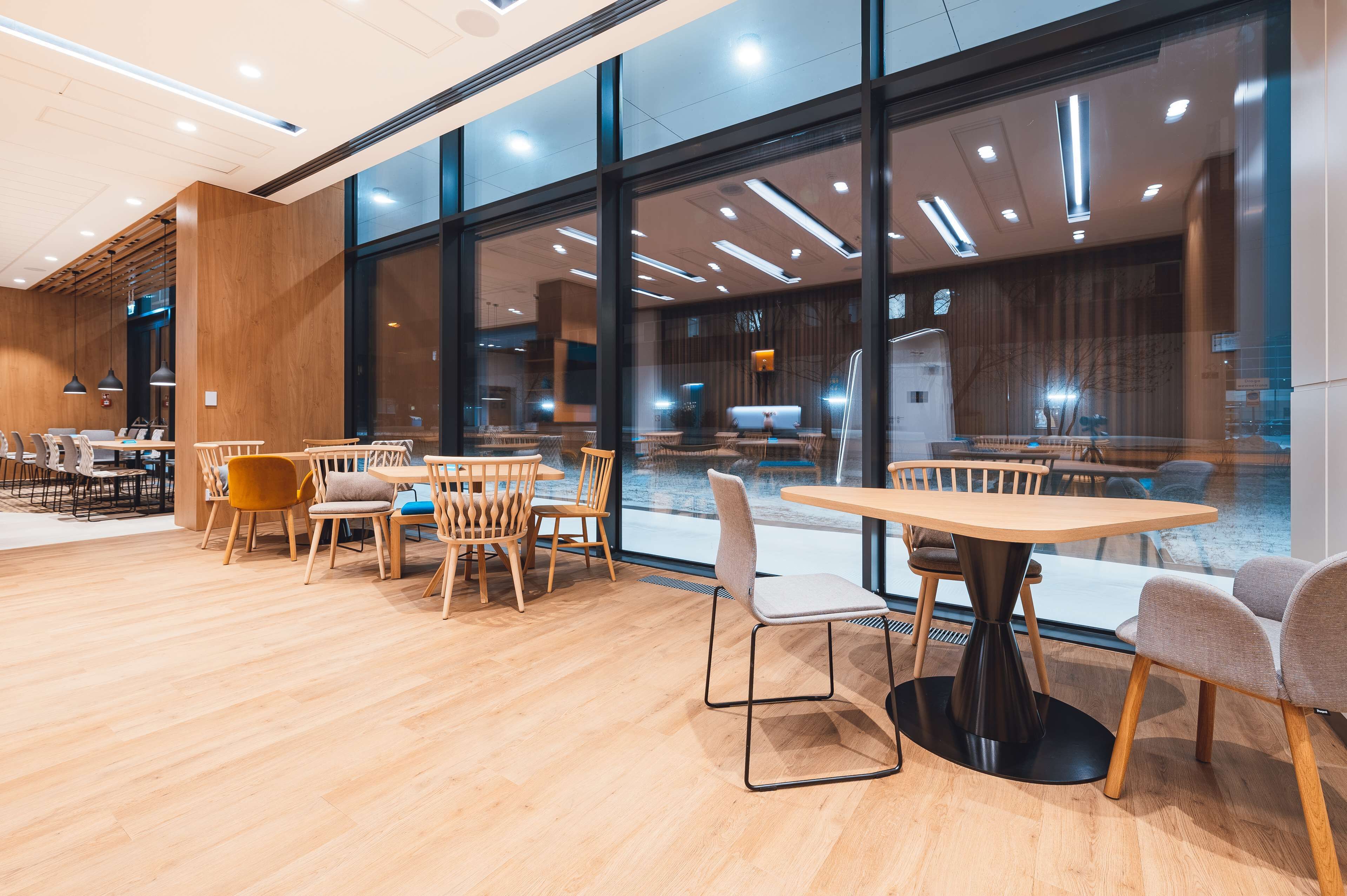 A modern indoor space with wooden flooring, round tables, and chairs.