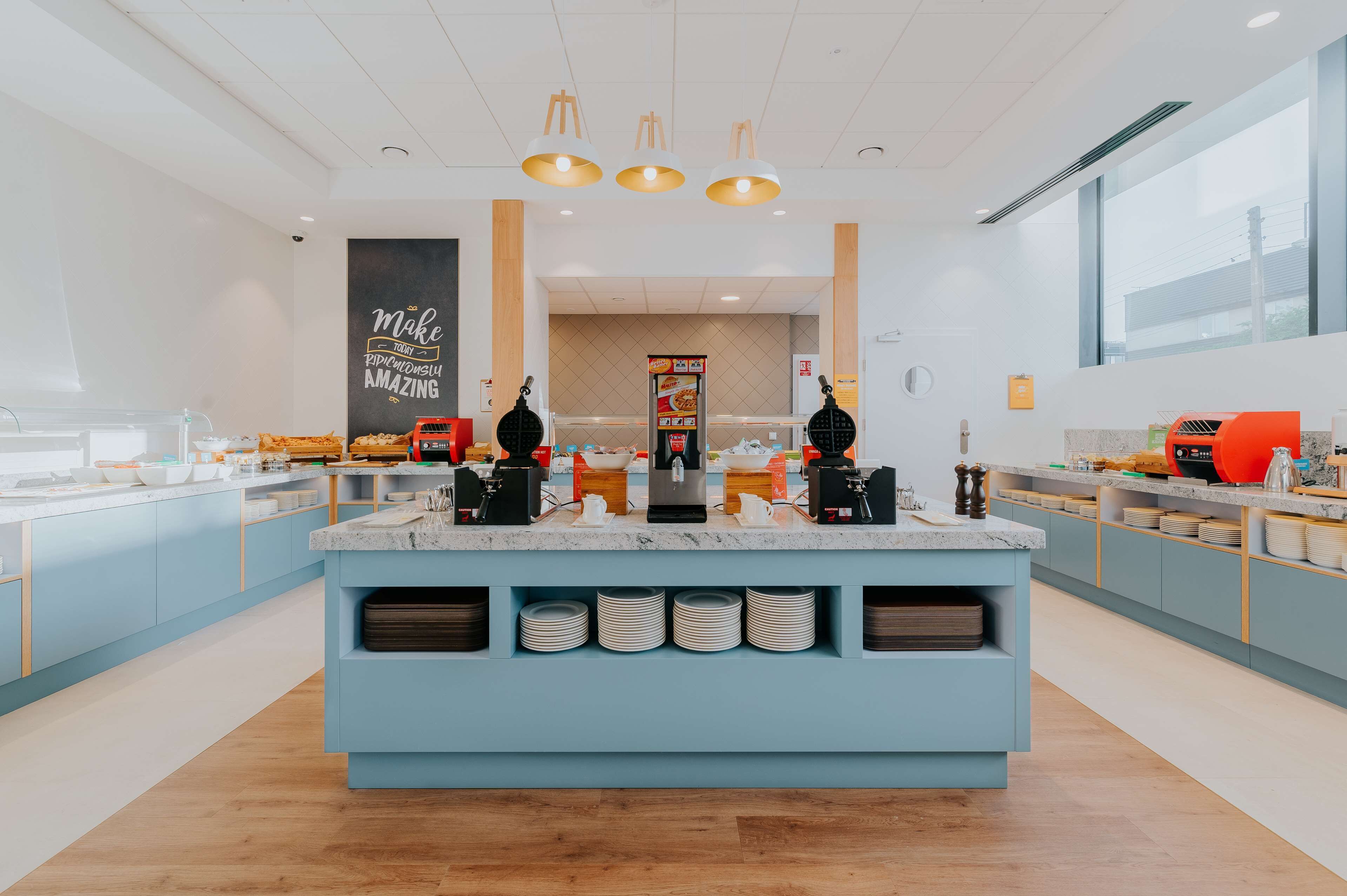 Une cuisine moderne dotée d’un îlot central, de meubles de couleur bleue et d’un mur décoré d’une citation inspirante.