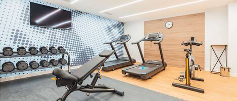 A gym with treadmills, a bench press, and a wall-mounted TV.