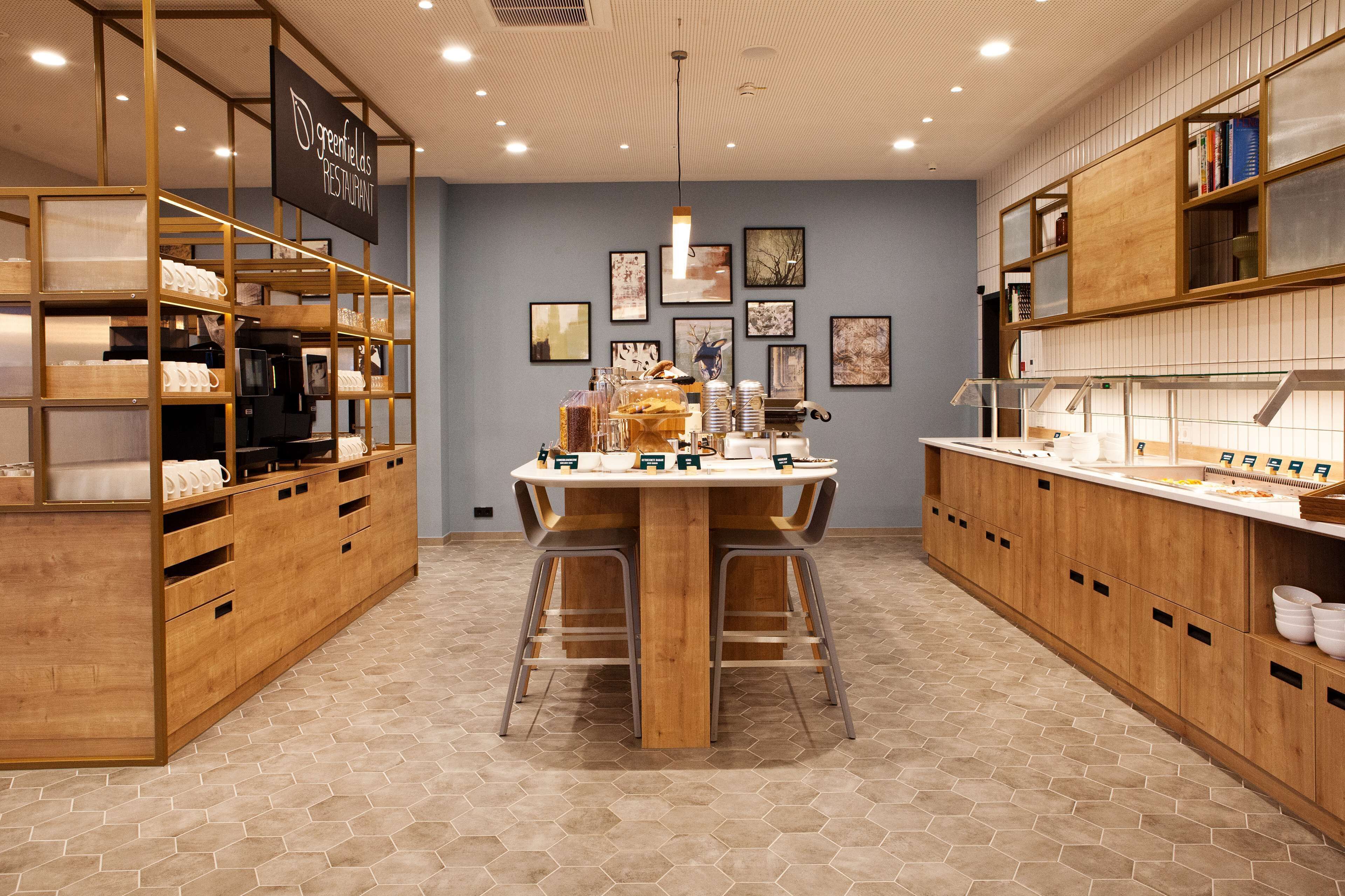 A modern restaurant interior with a central wooden table, hexagonal patterned floor, and wooden shelving units.