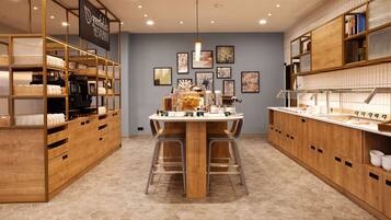 A modern restaurant interior with a central wooden table, hexagonal patterned floor, and wooden shelving units.