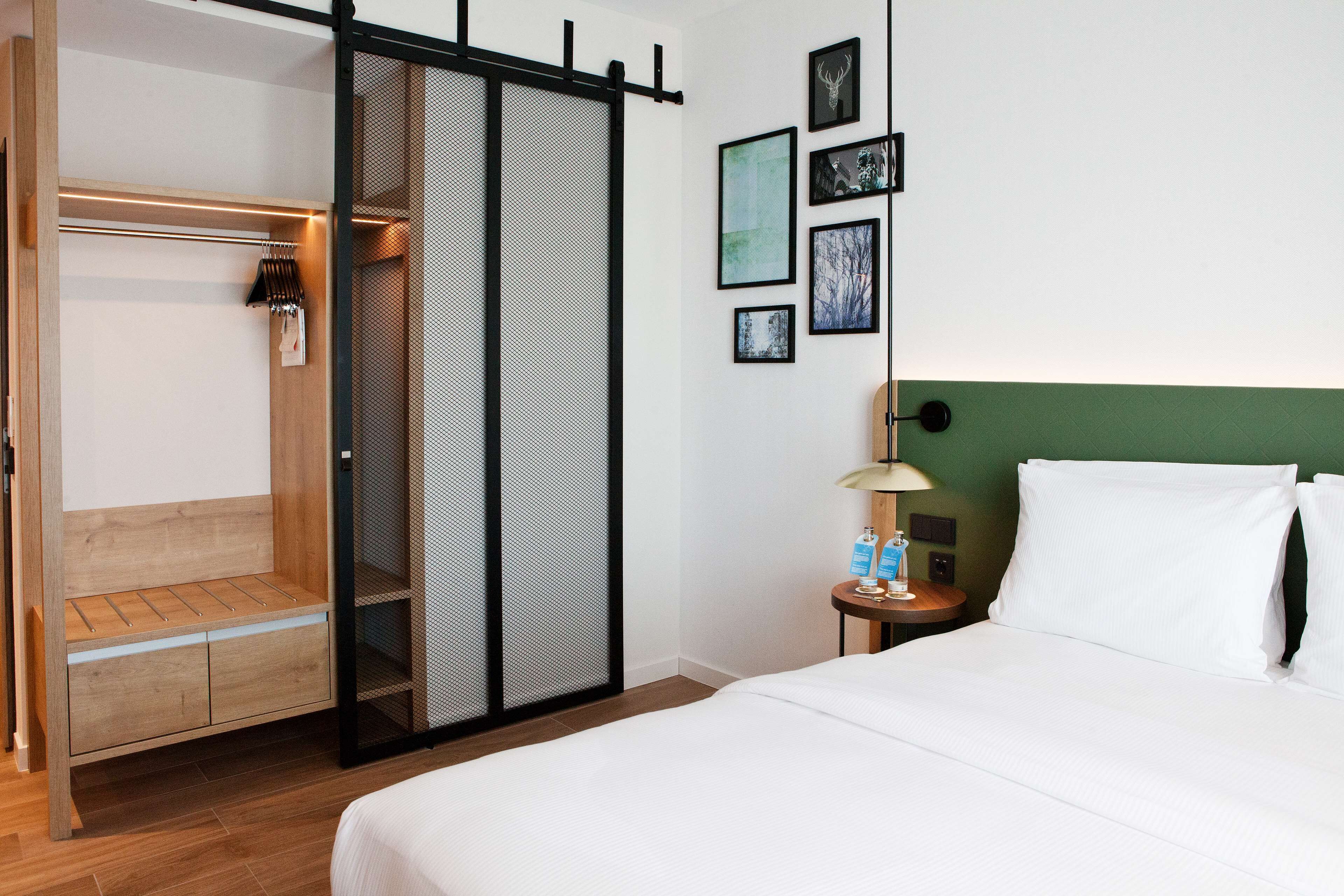 A hotel room with a bed, a wooden bench, a sliding door, and a wall with framed pictures.