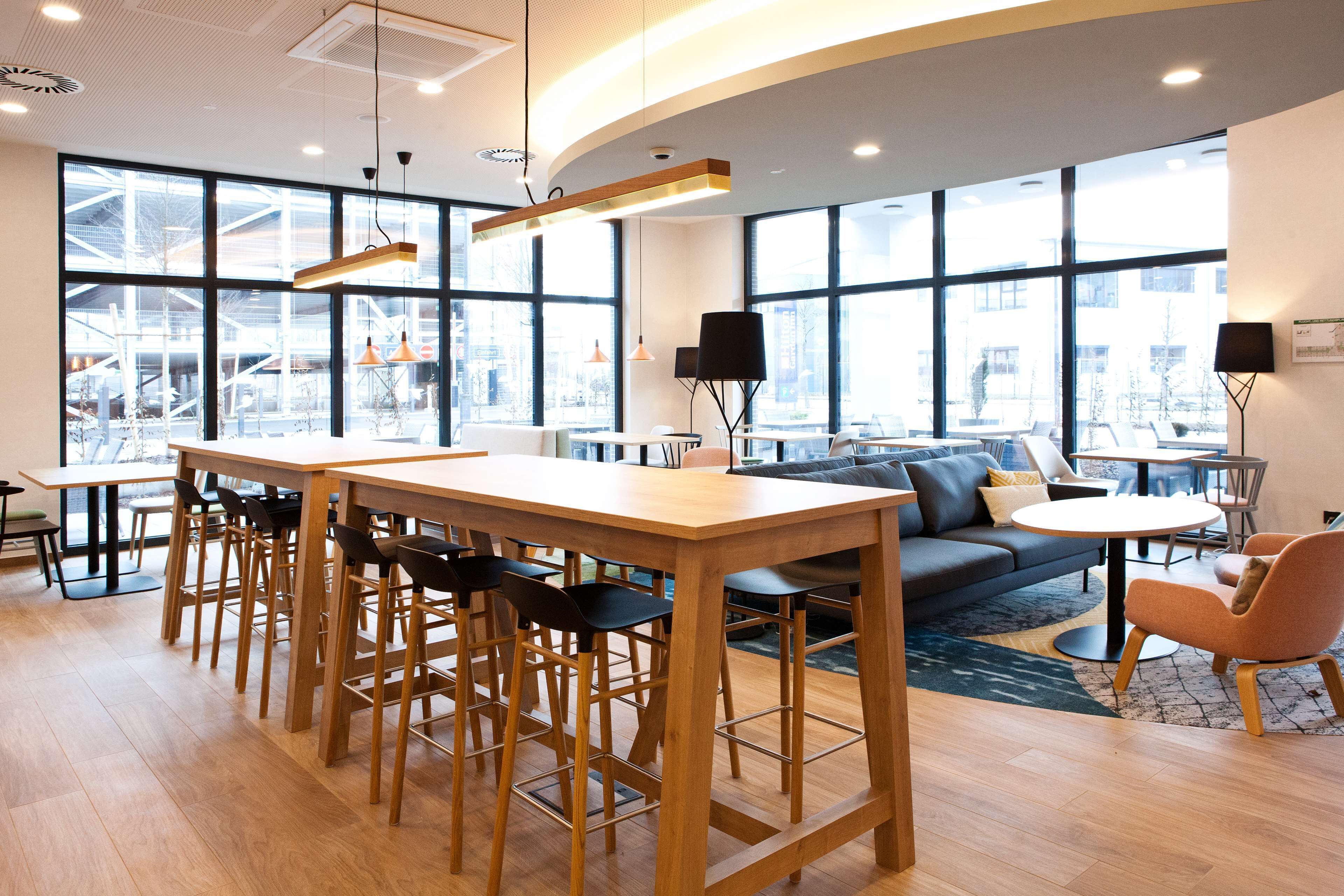 A modern interior with a wooden bar area, seating, and large windows offering views of the outside.