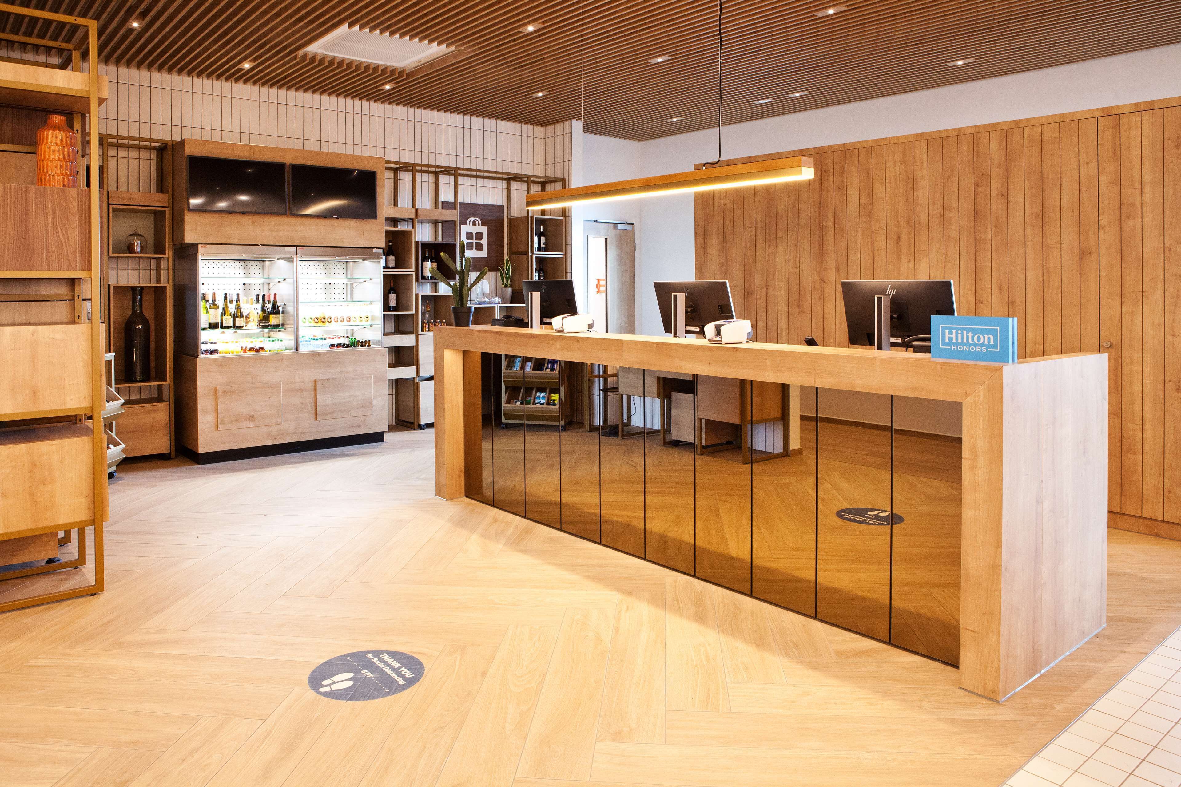 Zona de recepción de un hotel con un mostrador de madera, un minibar y un área de descanso con mesas y sillas.