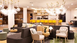 En modern hotellobby med en bardisk, sittgrupper och ett kök synligt i bakgrunden.