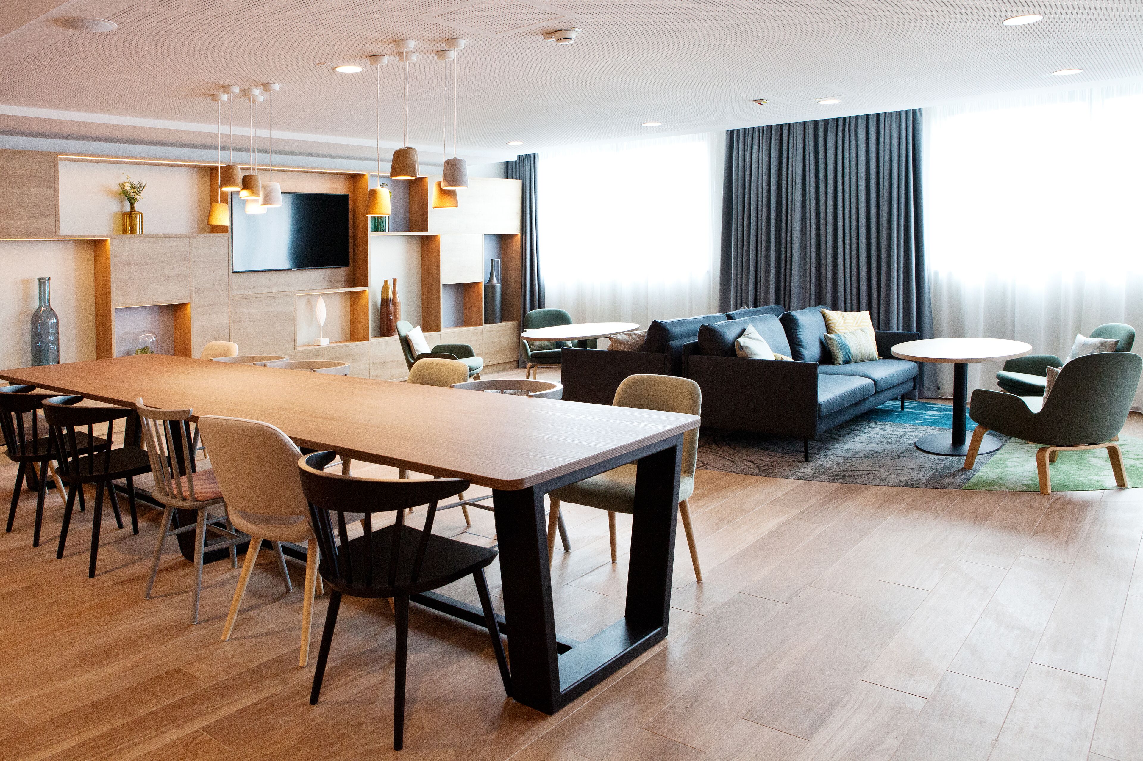 A modern hotel room with a dining area, a sofa, and a TV mounted on the wall.