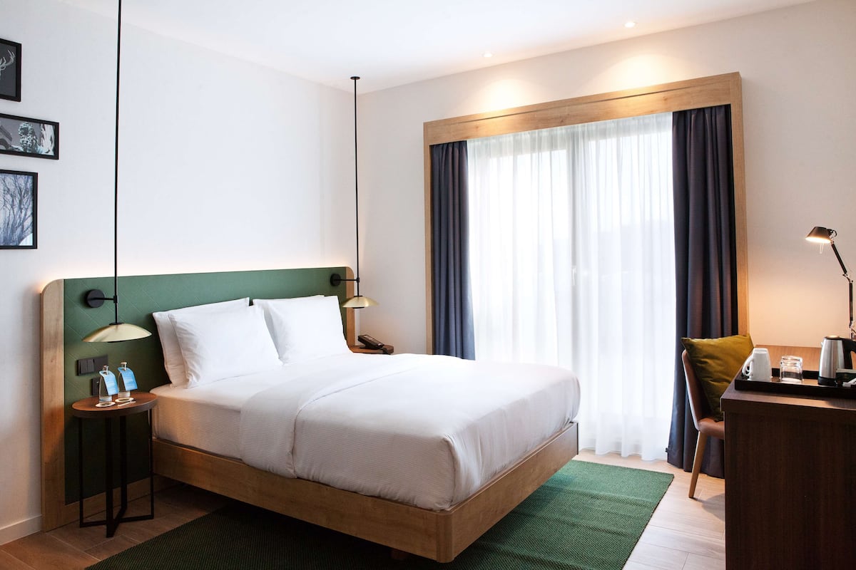 A neatly made bed with white linens, a wooden headboard, a bedside table with a lamp, and a chair with a tray of breakfast items.