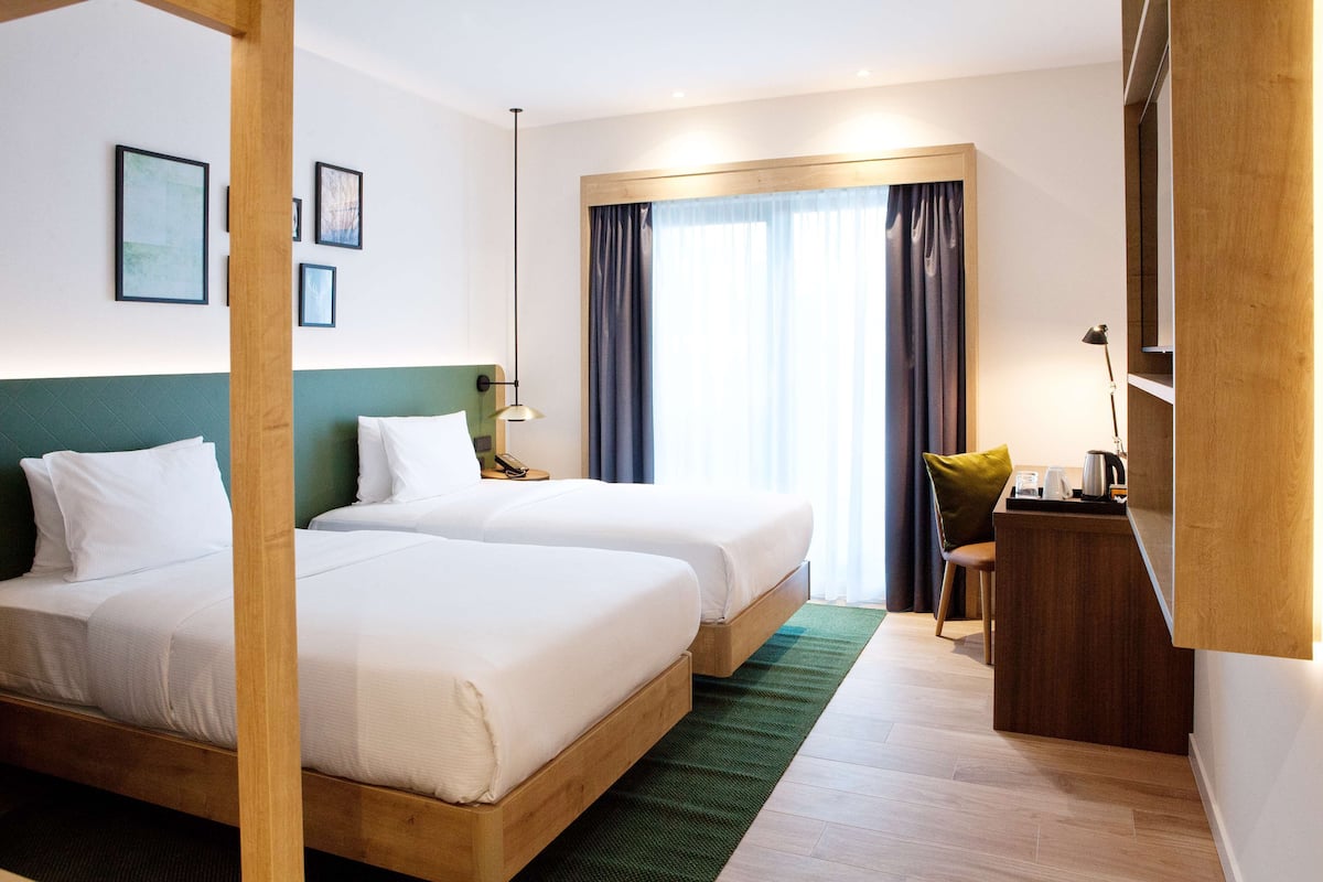 A hotel room with two beds, a desk, a chair, and a window with curtains.
