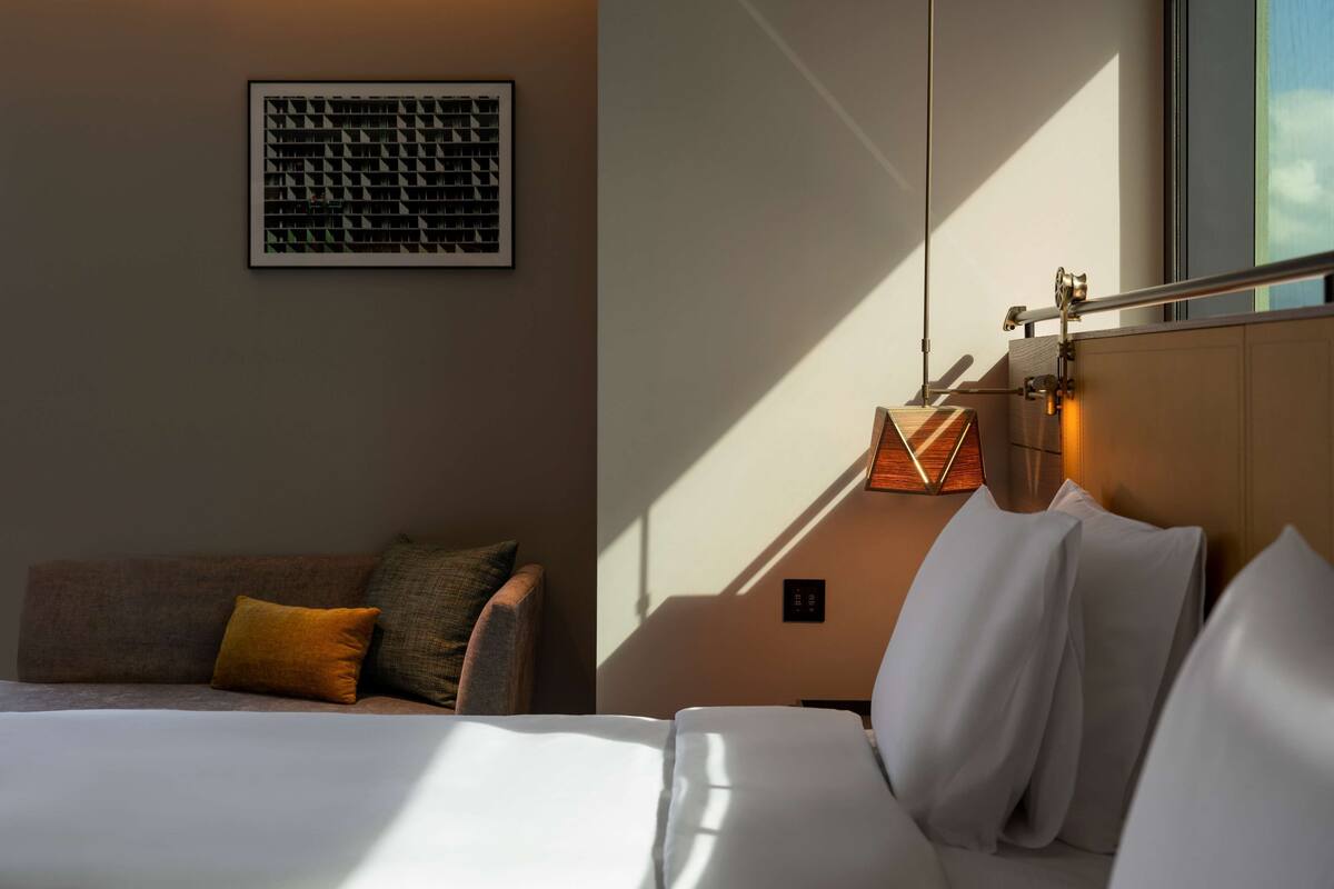 A hotel room with a bed, a nightstand, a lamp, a framed picture on the wall, and a window.
