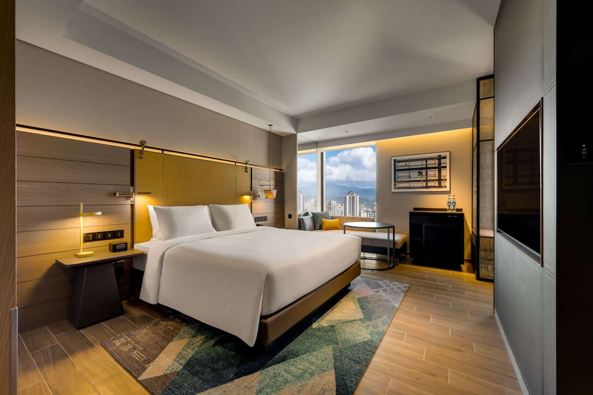 A modern hotel room with a large bed, bedside tables, a desk, and a view of the cityscape.