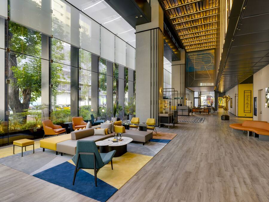 A spacious lobby with large windows, modern furniture, and a wooden floor.