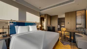 A modern hotel room with a large bed, a desk, a chair, and a small table.