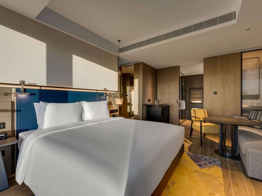A modern hotel room with a large bed, a desk, a chair, and a small table.