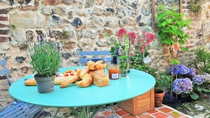 A round turquoise table with croissants, a glass of orange juice, and a potted plant. - LA MAISON BALANCOIRE - Private parking - private terrace - La Clé de Honfleur (Honfleur)