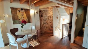 A cozy living room with a stone wall, a wooden staircase, a dining area with a swing chair, and a TV on a stand. - LA MAISON BALANCOIRE - Private parking - private terrace - La Clé de Honfleur (Honfleur)