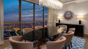 A dining area with a large oval table, six chairs, a chandelier, a round mirror, and a city view through large windows. - Hilton Mall of Istanbul (Istanbul)
