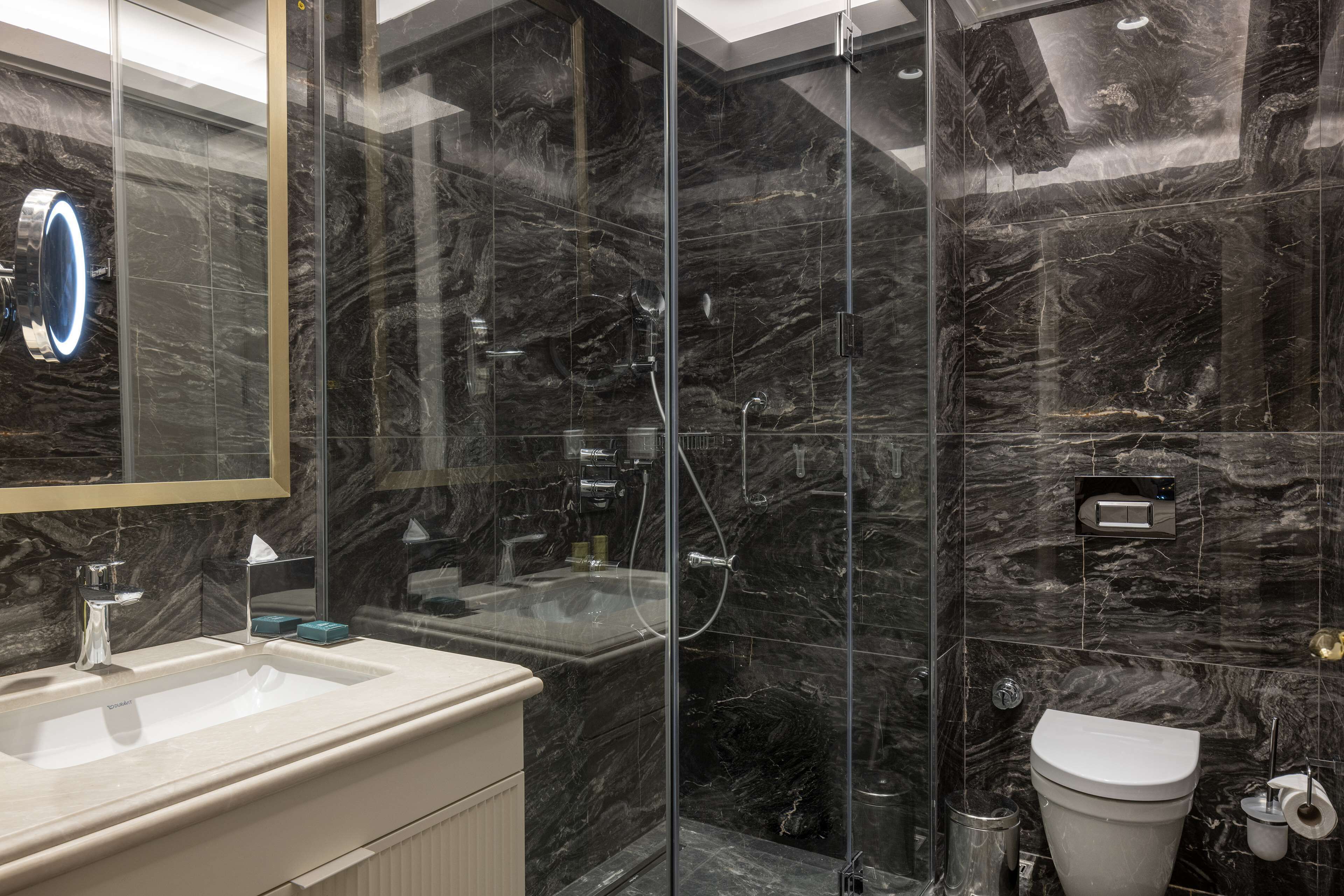 Un baño moderno con lavamanos de mármol, ducha con mampara de vidrio y un inodoro.