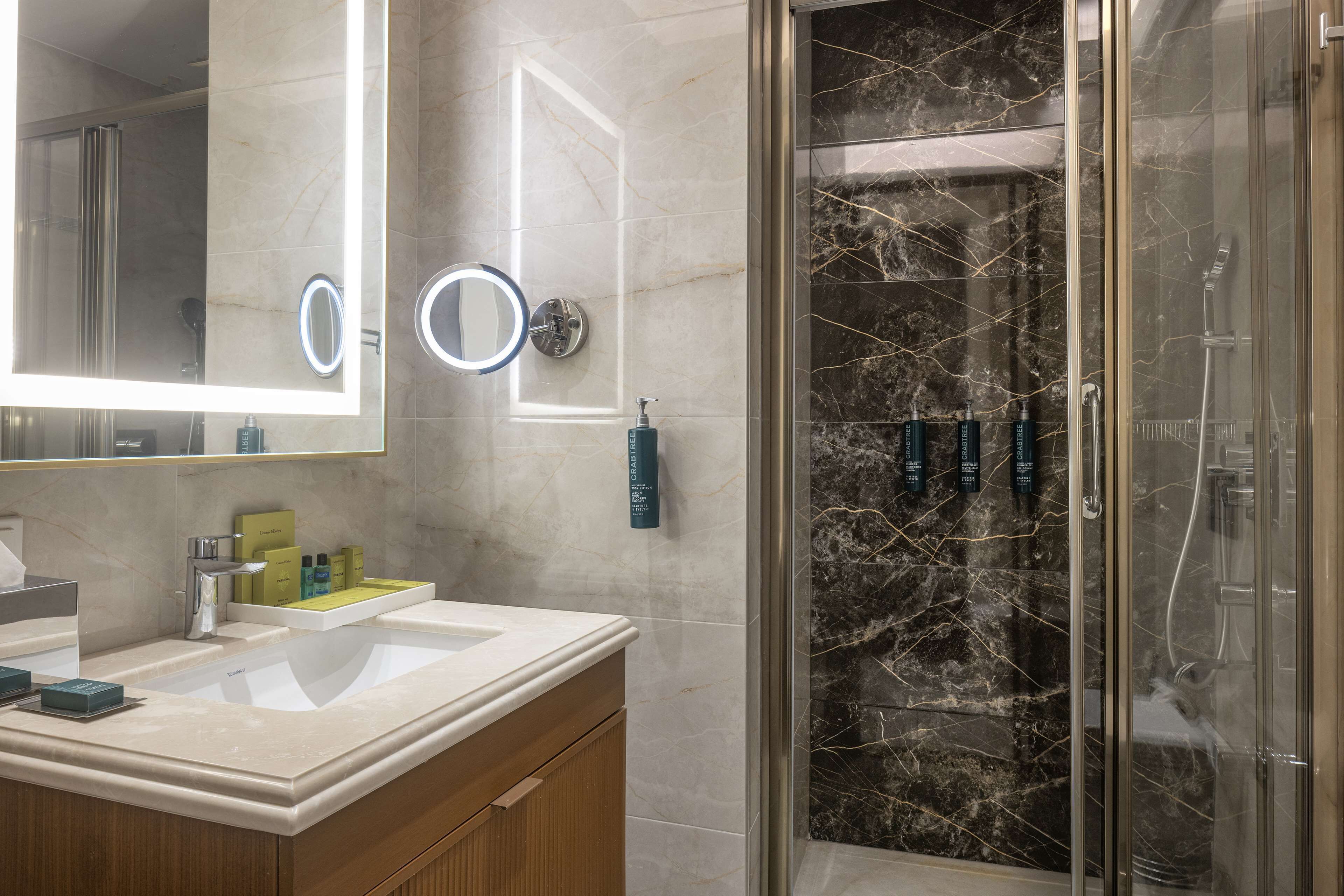 Un baño moderno con tocador de mármol, un espejo grande y una ducha con mampara de vidrio.