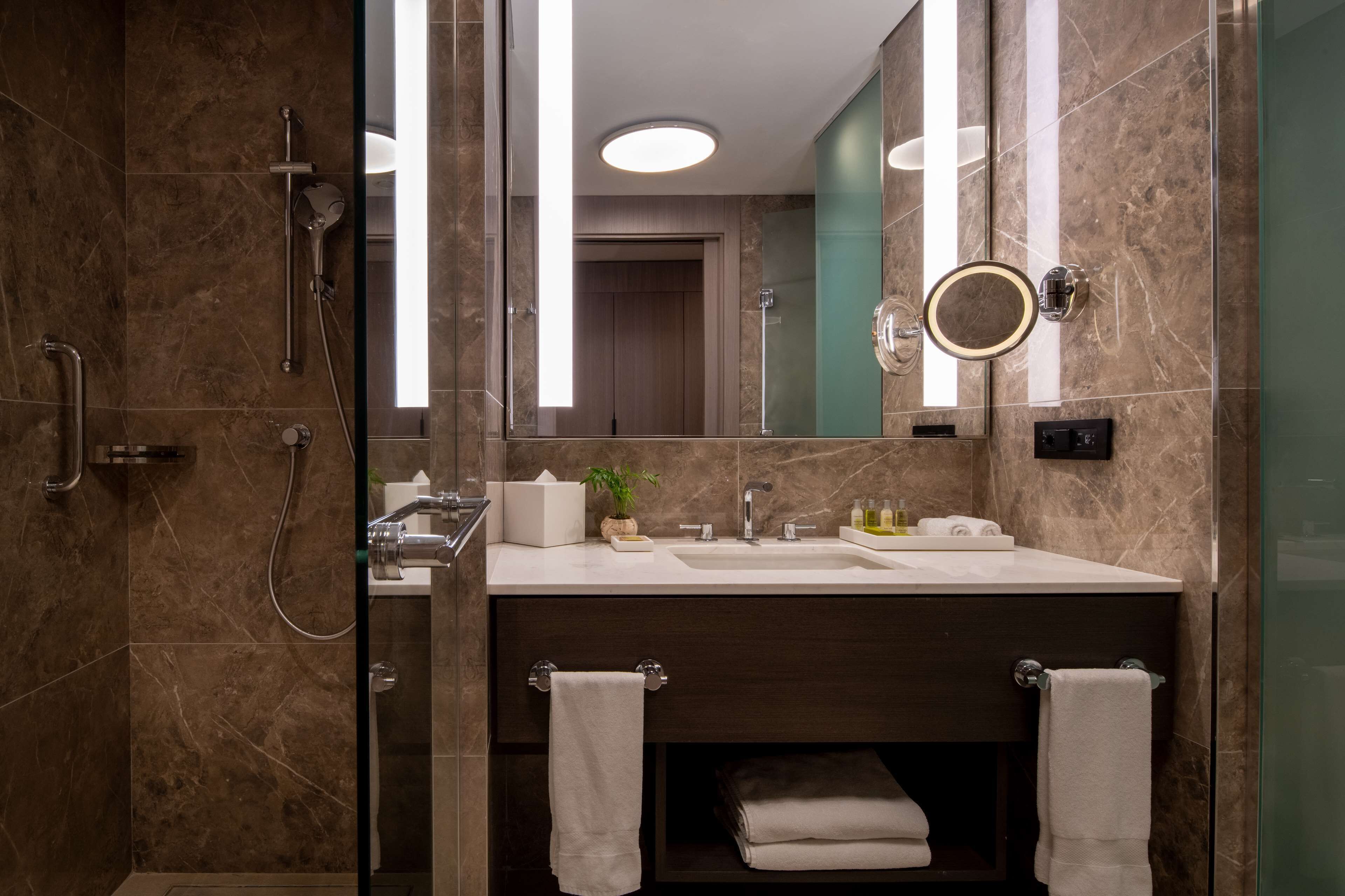 Un baño moderno con ducha de vidrio, un espejo grande y un lavamanos con toalleros.