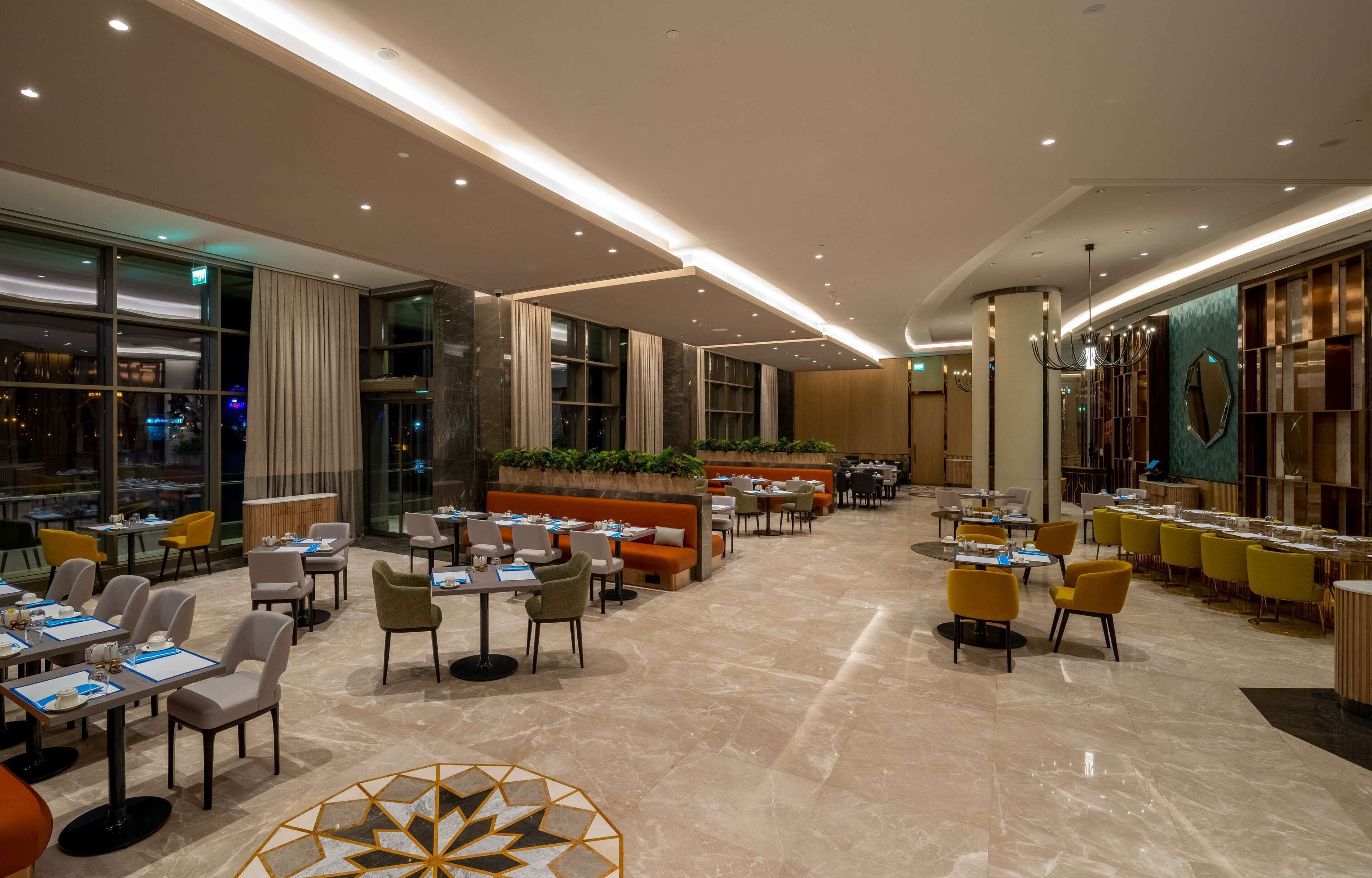 Un hall d’hôtel spacieux, doté de plusieurs espaces salon, notamment un long comptoir et plusieurs tables avec des chaises.