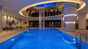 A modern indoor swimming pool with a central column, lounge chairs, and decorative wall art.