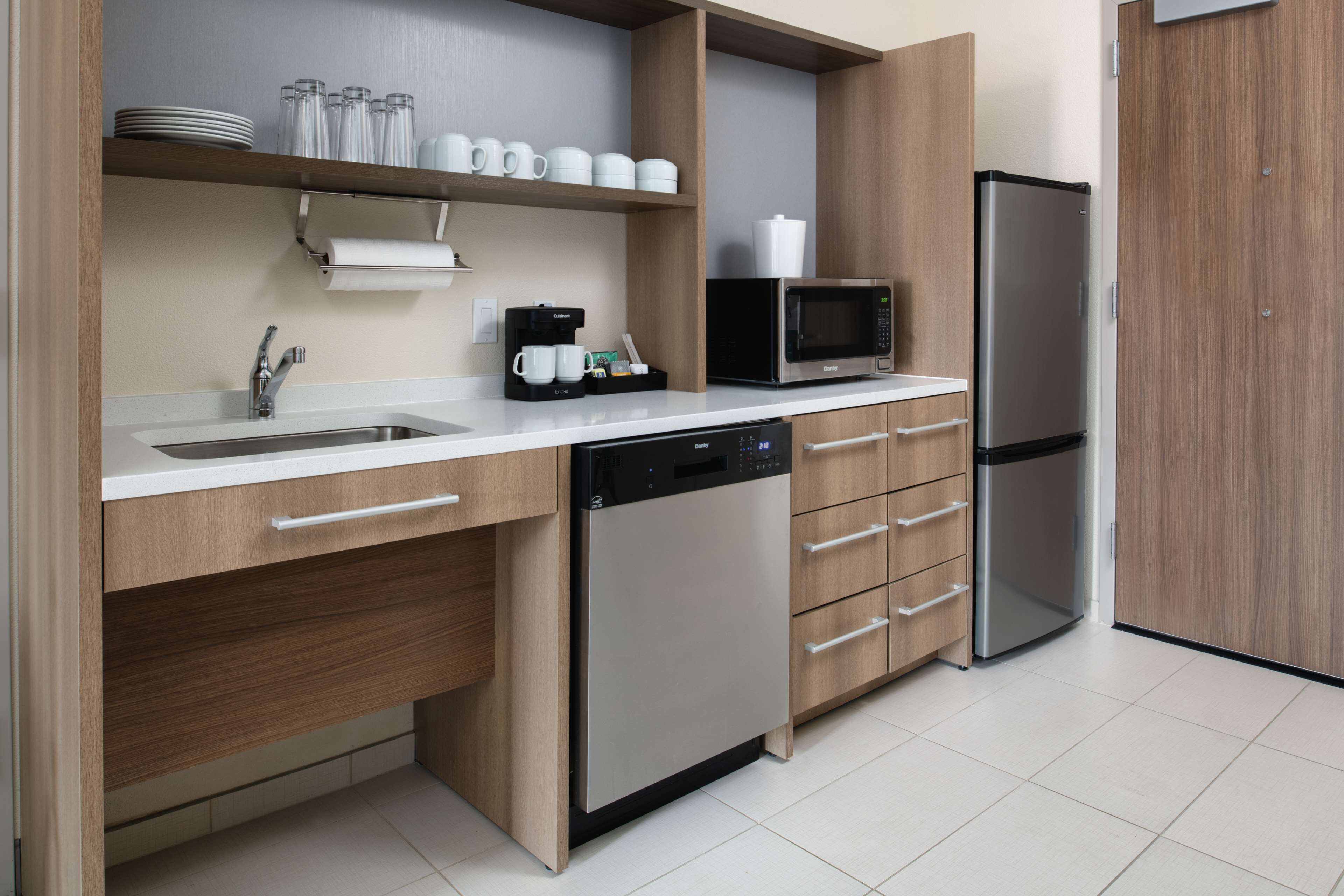 A modern kitchen with a dishwasher, microwave, refrigerator, and a coffee maker.