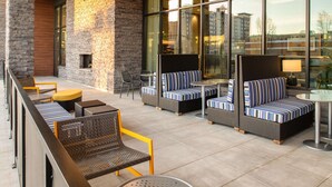 A modern outdoor seating area with wicker furniture and striped cushions, large windows offering city views, and a clean, tiled floor. - Home2 Suites By Hilton Boise Downtown (Boise)