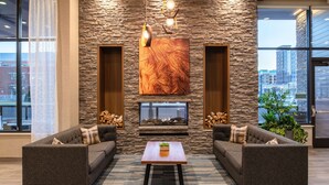 A modern living room with a stone wall, a fireplace, two sofas, and a coffee table. - Home2 Suites By Hilton Boise Downtown (Boise)