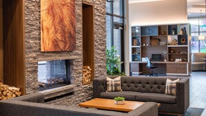 A modern living room with a stone fireplace, a grey sectional sofa, and a wooden coffee table. - Home2 Suites By Hilton Boise Downtown (Boise)