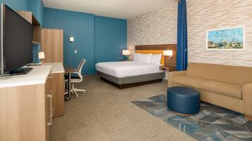 A hotel room with a bed, a desk with a computer, a chair, a sofa, and a TV.