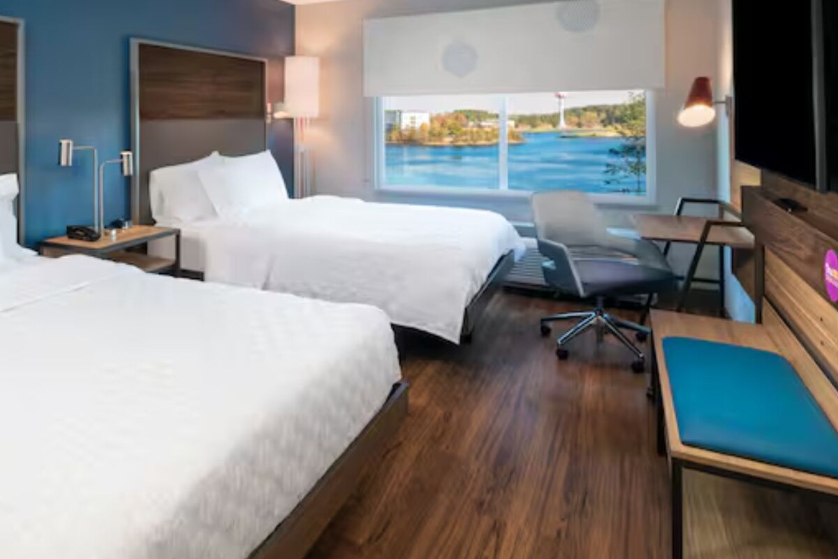 Een hotelkamer met twee bedden, een bureau, een stoel en een groot raam met uitzicht op het water.