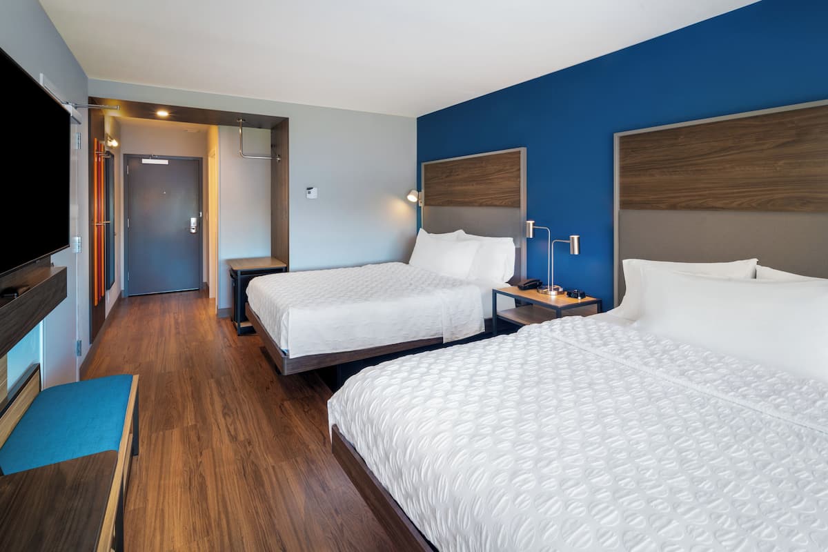 Habitación de hotel con dos camas, televisión y suelo de madera.