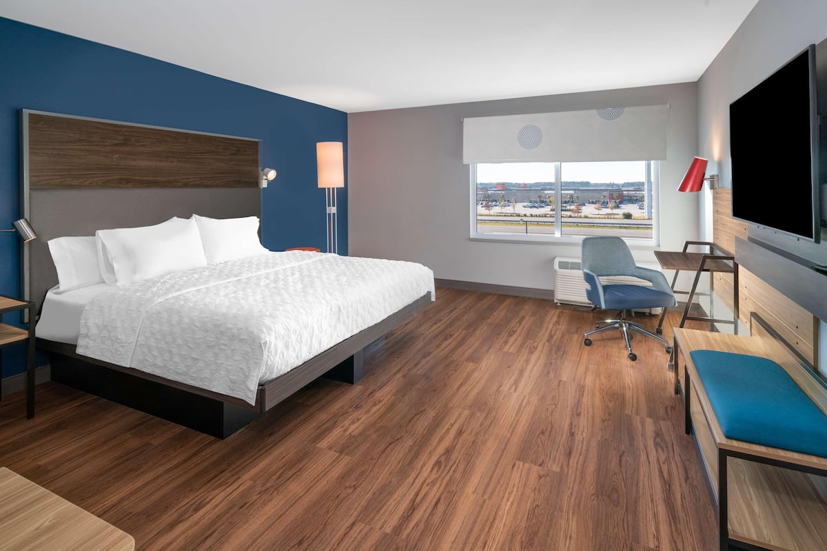 Una habitación de hotel moderna con una cama, un escritorio, una silla, un televisor y una ventana con vistas a la ciudad.